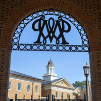 A wrought-iron W&M cypher sits atop a brick archway with a building visible in the background