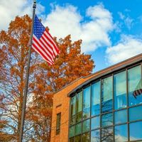 A flag pole with an American flag outside of a brick building with large windows