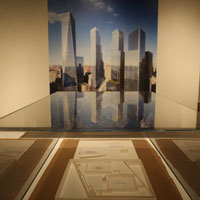 A large photo of the World Trade Center memorial on the wall behind a glass case containing flat white architectural models related to the site.