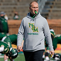 A coach walks through football practice with whistle in mouth