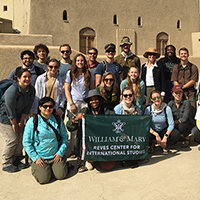 Students stand outside a castle holding a William & Mary banner