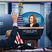 Jen Psaki stands at the lecturn of the White House briefing room