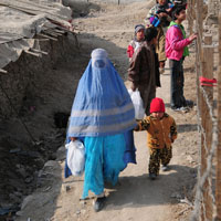 A woman holding a bag and her child walk near a fence (NATO photo)