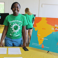 A person wearing a shirt saying "I studied abroad" stands behind a table with a poster showing India on it