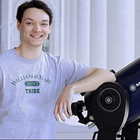 Student wearing W&M shirt leans against a telescope 