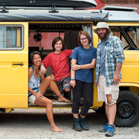 Four people stand beside and sit in a yellow van