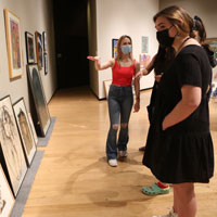 People looking at paintings on walls as one person gestures towards artwork