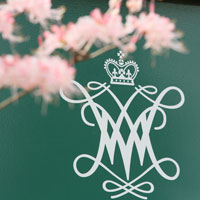 Green sign with white W&M cypher and pink cherry blossoms hanging in front of it