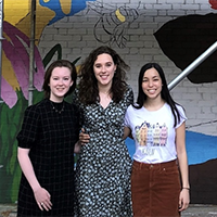 Three students stand in front of mural 