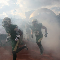 Football players run through smoke as they enter the field