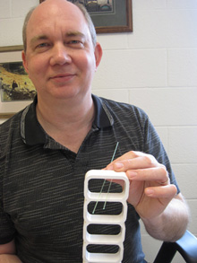 W&M physicist Jeff Nelson holds a teeny sliver of one of the NOvA detector’s PVC extrusions, showing how optical fibers are routed through each mineral-oil-filled chamber. The assembled far detector will be 50 x 50 x 255 feet. Photo by Joseph McClain.
