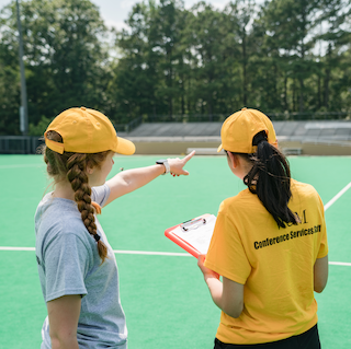 two summer staff members in yellow conference & events gear survey a field.