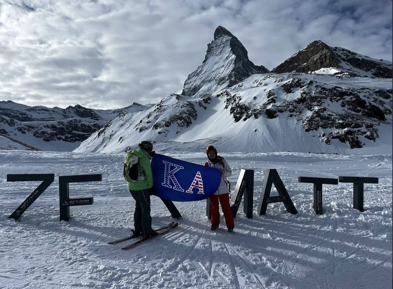 Two Kappa Alpha brothers hold up the fraternity flag at the top of a mountain.