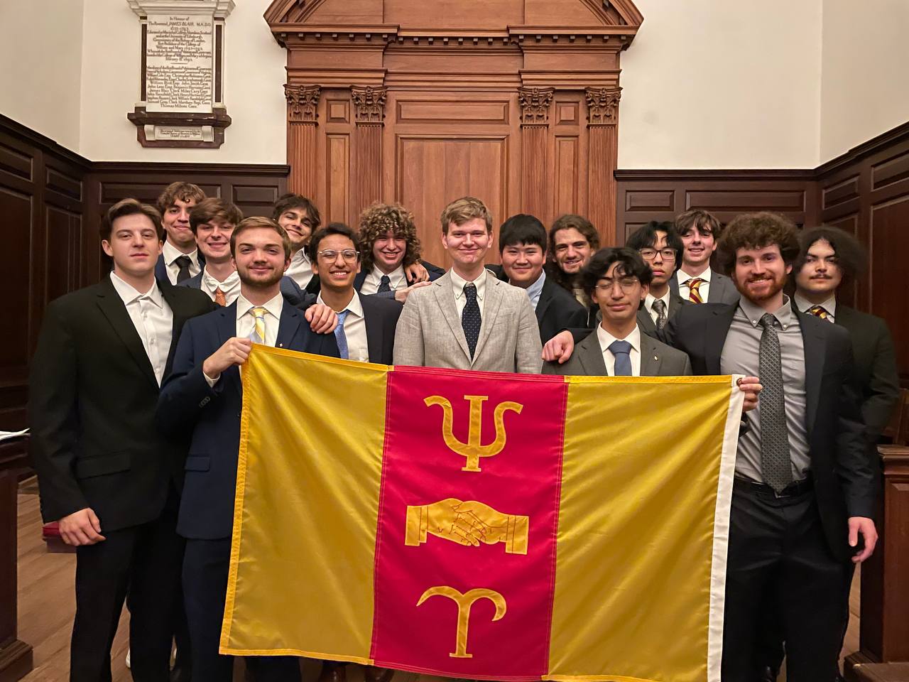 Psi Upsilon brothers pose in front of their fraternity flag.