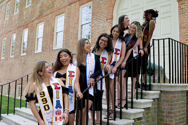 Hermandad de Sigma Iota Alpha, Inc. members pose for a photo on stairs, wearing their graduation stole.