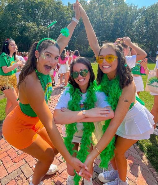 Smiling Thetas in festive attire and green boas on bid day in the Sunken Garden