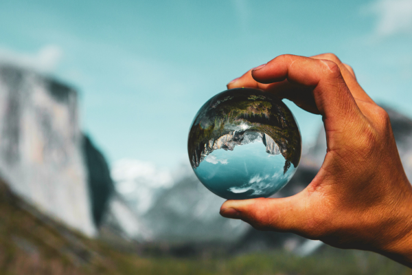 A hand holds a crystal ball in front of a scenic mountain skyline.