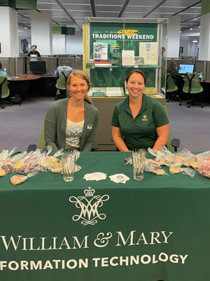 Erin Fryer and Melissa Palacios sit at a table with giveaways in Swem Library during finals. 