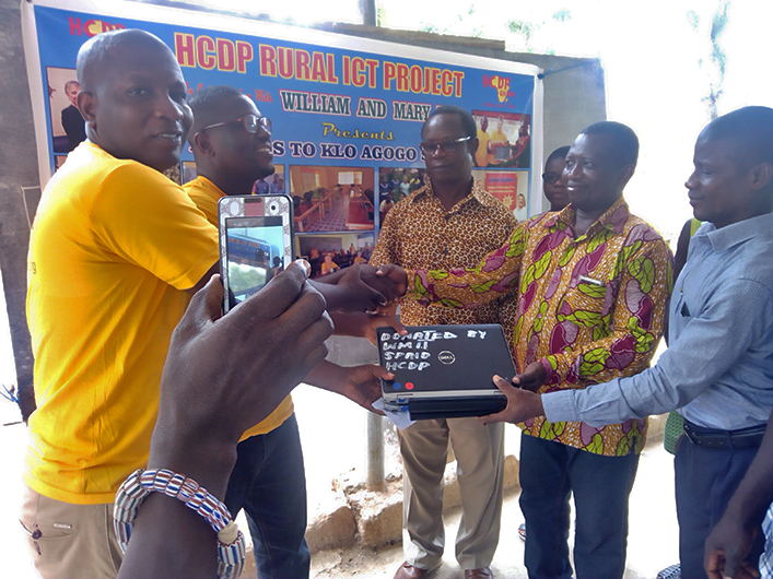 In front of the HDCP banner, volunteers exchange laptops with students