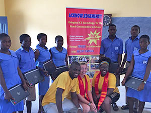 William & Mary students pose with HDCP workers and Ghanaian students at a previous laptop exchange in 2017. Behind them is a poster highlighting IT's contributions through the laptop exchange program.