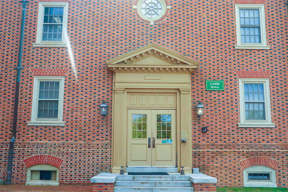 The double door entrance of a brick, windowed dorm building.