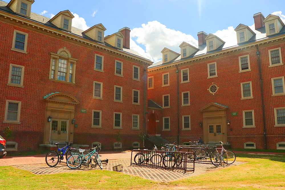 There are two entrances to a brick, windowed dorm building with four bike racks in between.