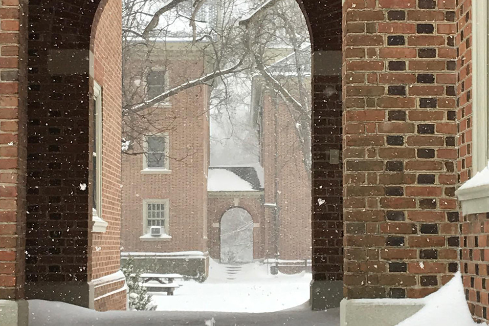 A snowy, arched walkway leads to a brick, windowed dorm building.