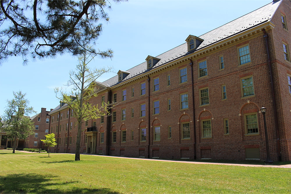 Brick, windowed dorm building surrounded by a vast green lawn.