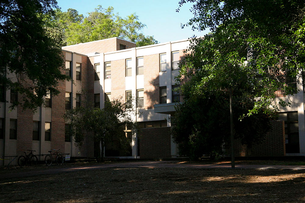 Brick, windowed dorm building nestled in greenery.