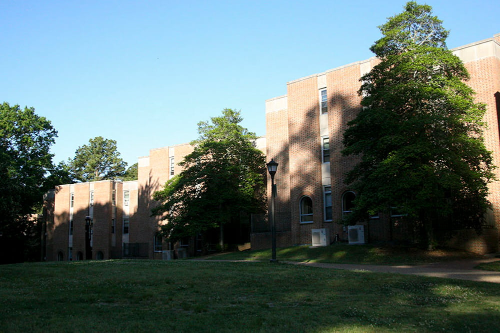 Brick building in a grassy area with large trees nearby