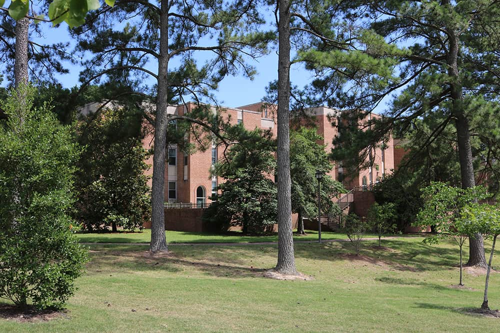 Brick building in a grassy area with large trees nearby