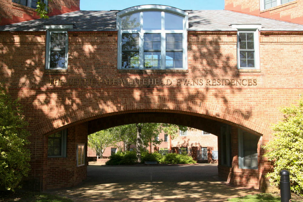 Brick building with the lettering The Lettie Pate Whitehead Evans Residences lettering over an arched entrance to a brick courtyard with trees