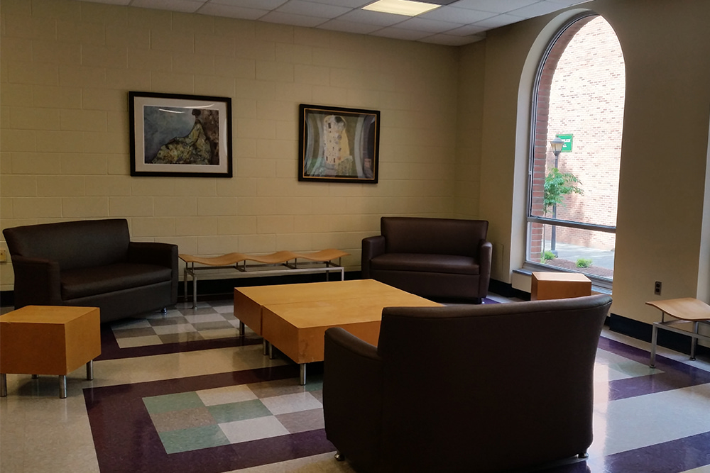 Common room with seats, side tables, coffee table, art, and large window. 