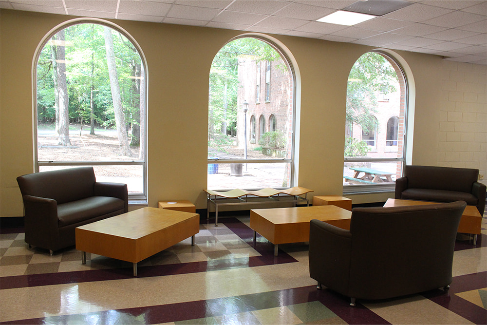 Another view of the common area, featuring seating, tables, and large arched windows. 