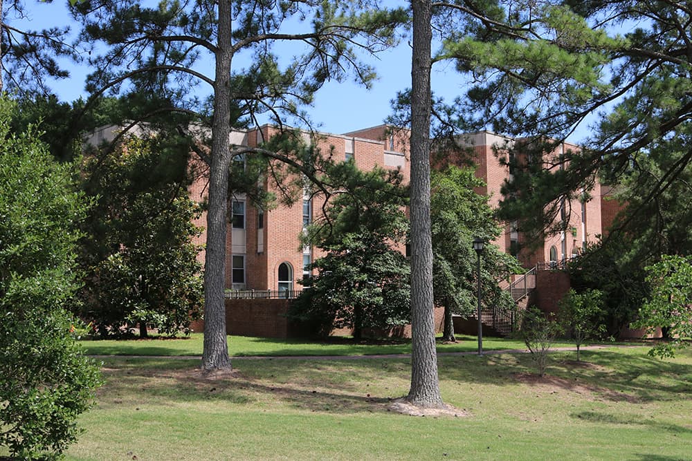 Brick residence hall in a grassy area with large trees nearby