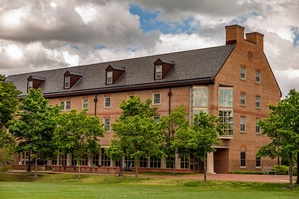 Brick, windowed dorm building surrounded by a walkway and green lawn.