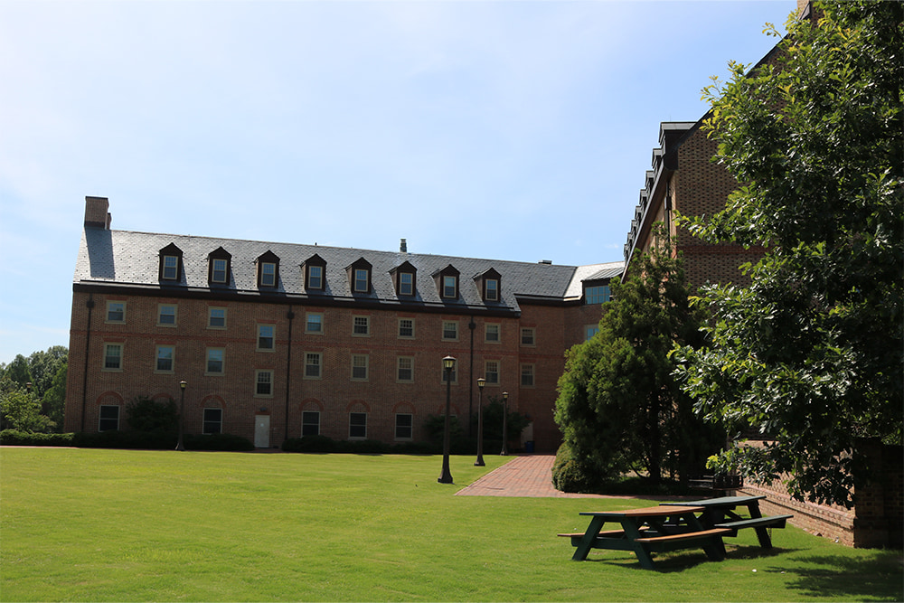 Brick, windowed dorm building surrounded by a vast green lawn.