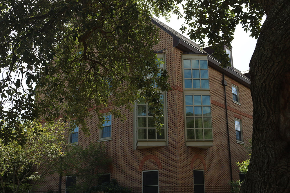 Brick dorm building with a large, windowed space nestled in greenery.