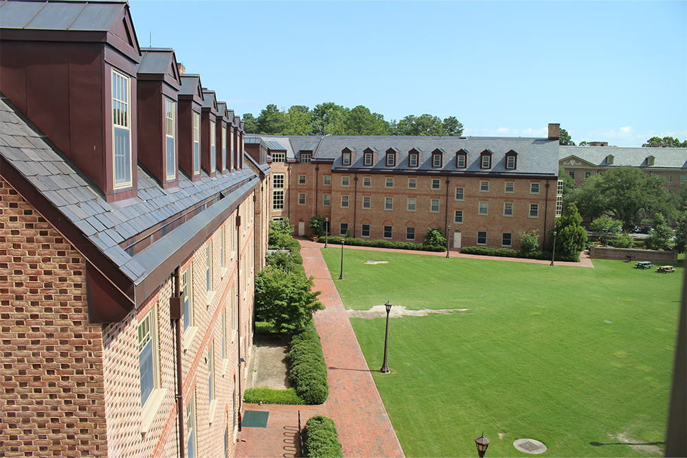 Aerial view of a brick, windowed dorm building surrounded by a vast green lawn.
