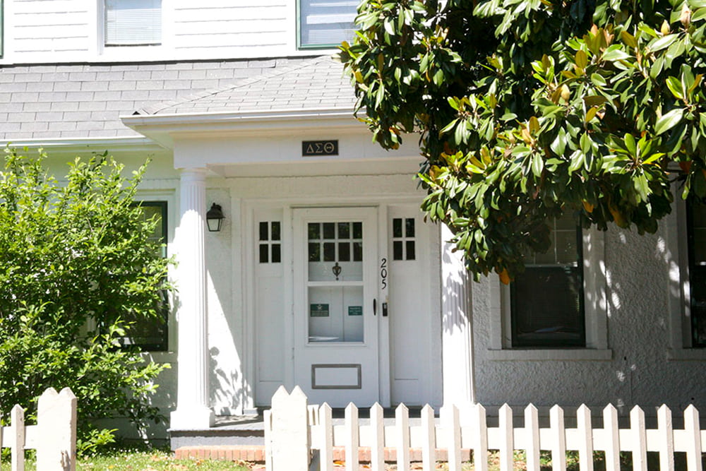 An historic house with white siding with a large Magnolia tree in front