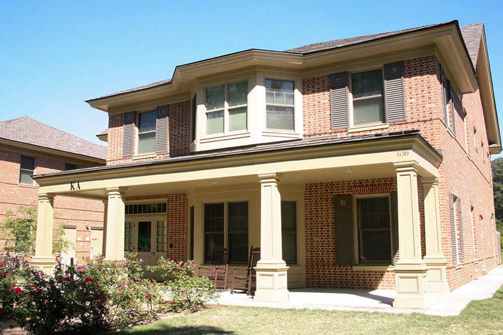 Brick fraternity house with a front porch and flowering bushes