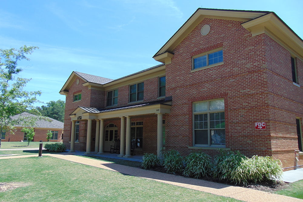 Brick fraternity house with a front porch and flowering bushes