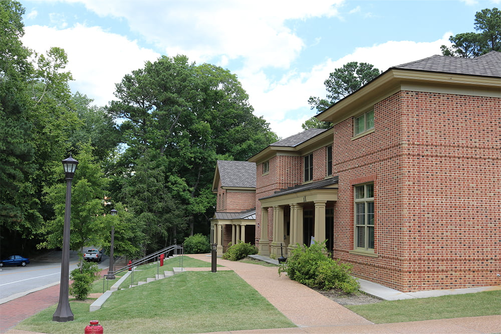 Brick fraternity house in a row with other houses along a street with brick walkways, trees and shrubs