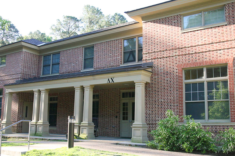 Brick fraternity house with a front porch and flowering bushes