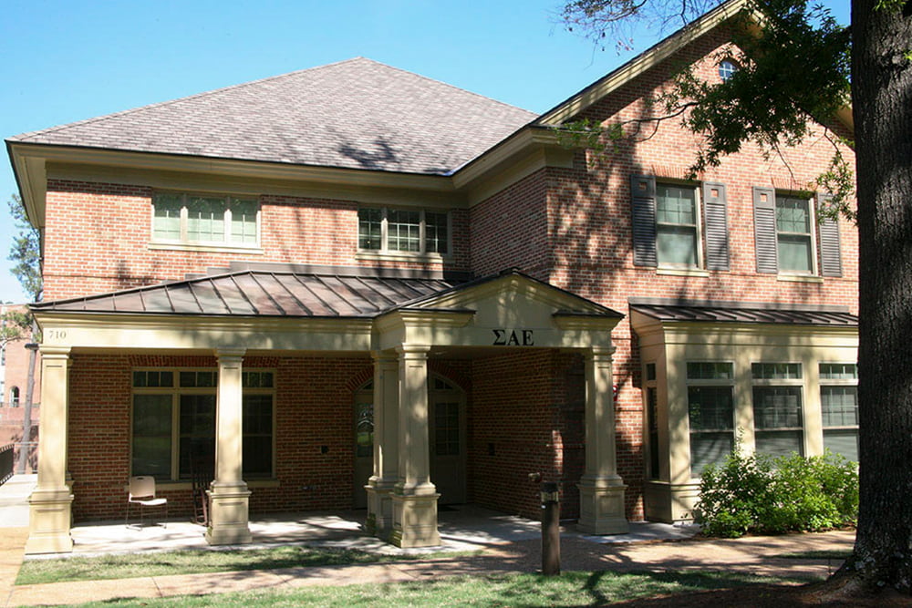 Brick fraternity house with a front porch and shrubs