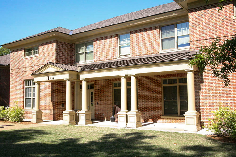 Brick fraternity house with a front porch and bushes