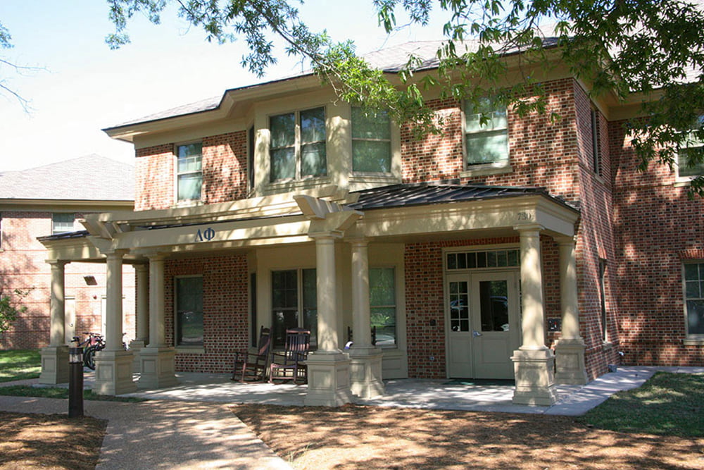 Brick fraternity house with a front porch nestled in the trees