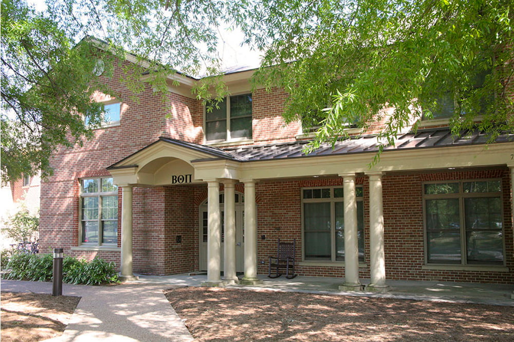 Brick fraternity house with a front porch nestled in the trees