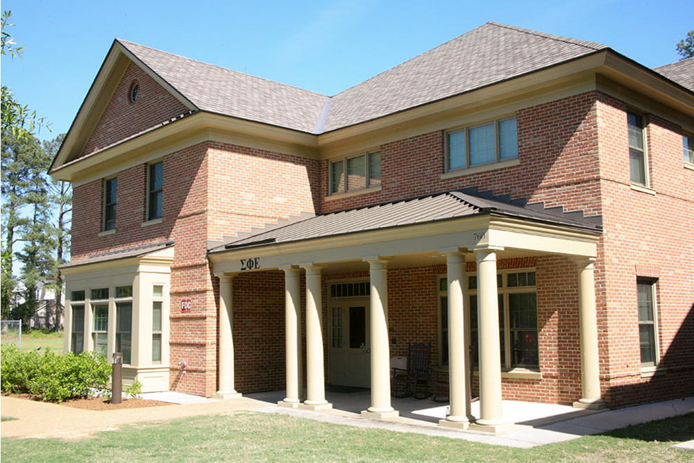 Brick fraternity house with a front porch and bushes