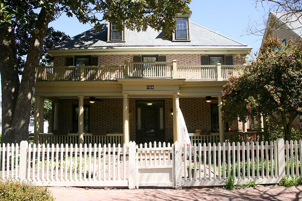 An historic brick house with dormer windows, double front porch and white picket fence containing a small front yard